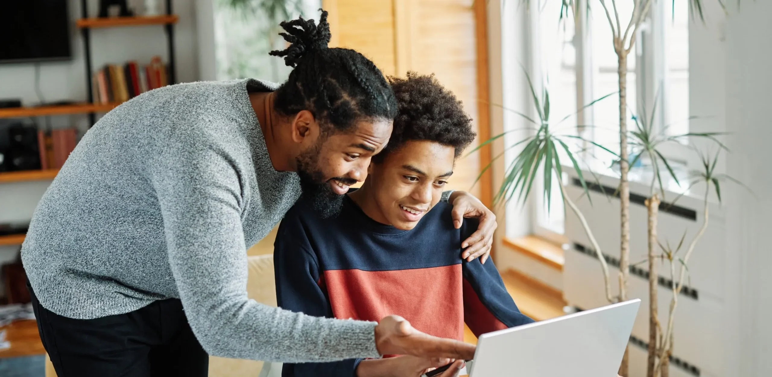 Young man showing younger boy something on laptop