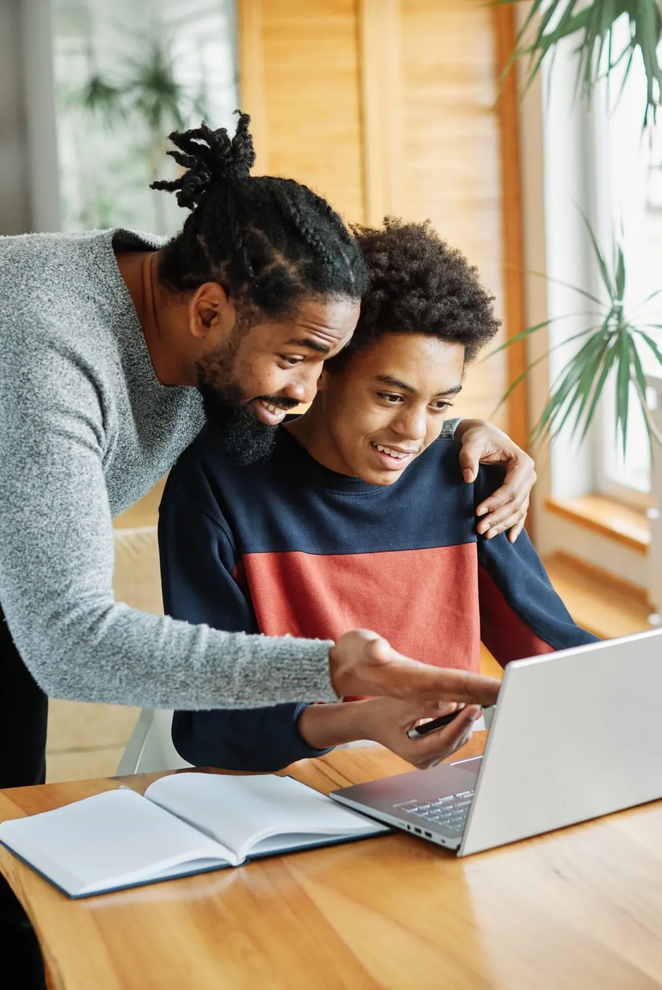 Young man showing younger boy something on laptop